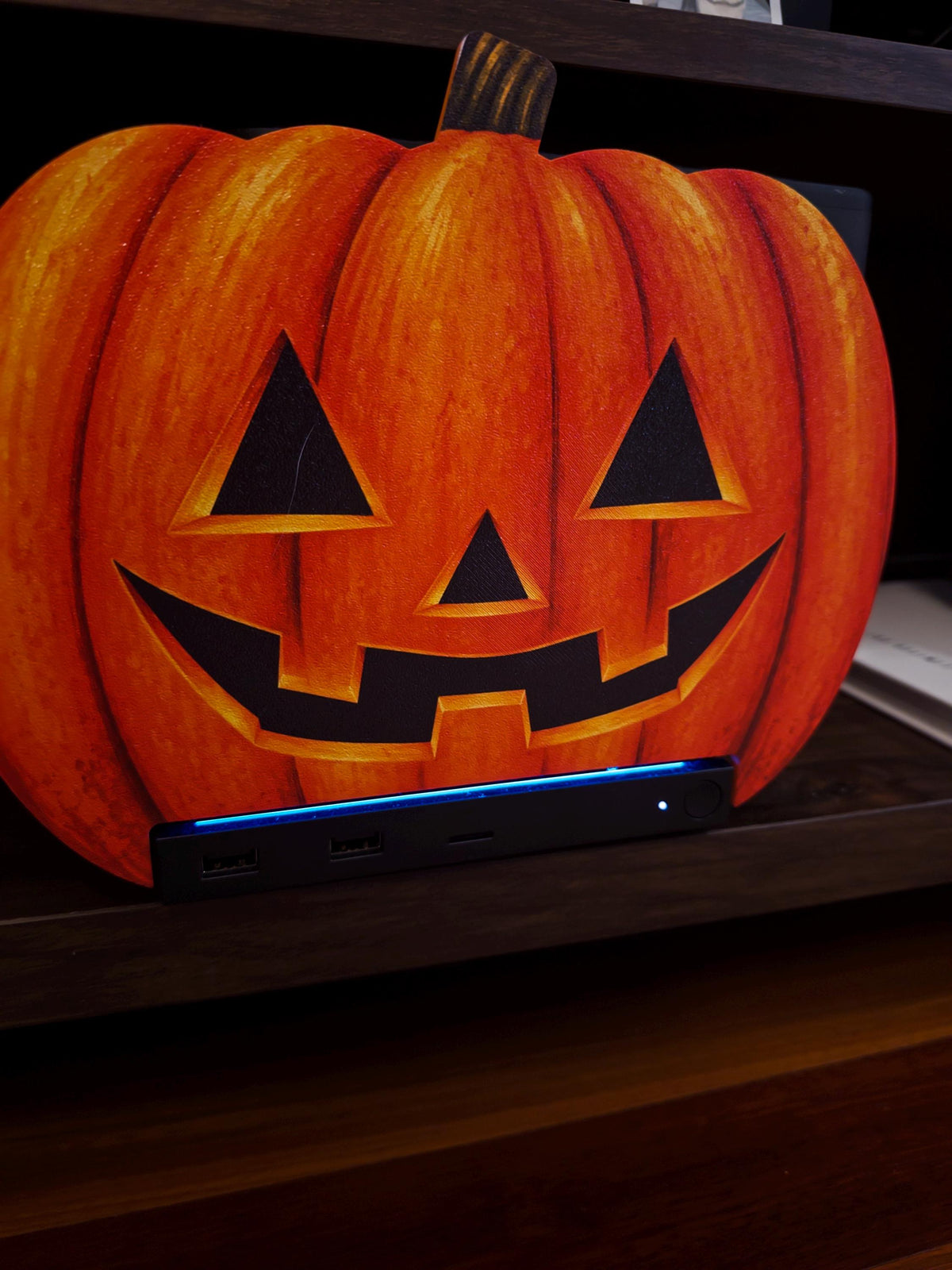 Steam Machine Faceplate Halloween Pumpkin, Classic or Cute Jack o Lantern Magnetic Plate, UV Printed Console Cover, Spooky Gamer Gif, close-up of the classic carved jack-o-lantern pumpkin faceplate installed on the Steam Machine on a dark wooden shelf, with the console's blue light strip glowing below