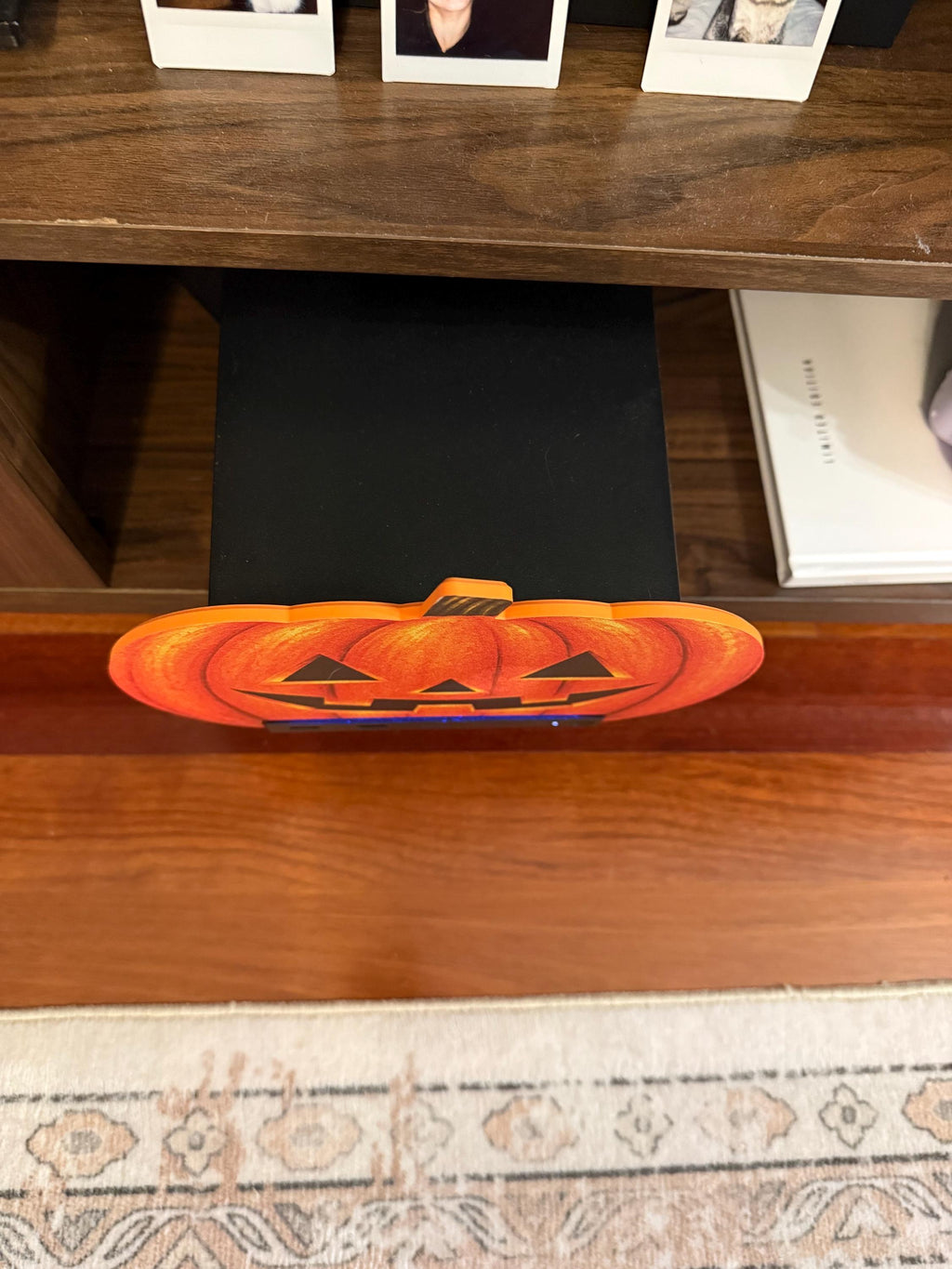 Steam Machine Faceplate Halloween Pumpkin, Classic or Cute Jack o Lantern Magnetic Plate, UV Printed Console Cover, Spooky Gamer Gif, top-down view of the classic carved jack-o-lantern pumpkin faceplate installed on the Steam Machine inside a wooden media cabinet, with framed cat photos on the shelf above and a patterned rug below
