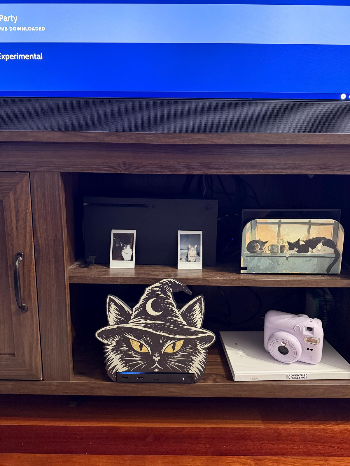 Steam Machine Faceplate Black Cat Witch Hat, Halloween Witchy Cat Magnetic Plate, UV Printed Console Cover, Spooky Gamer Gift, black cat witch hat faceplate installed on the Steam Machine on a wooden media cabinet shelf beside a pink instant camera, with a TV above and small framed cat photos on the shelf above