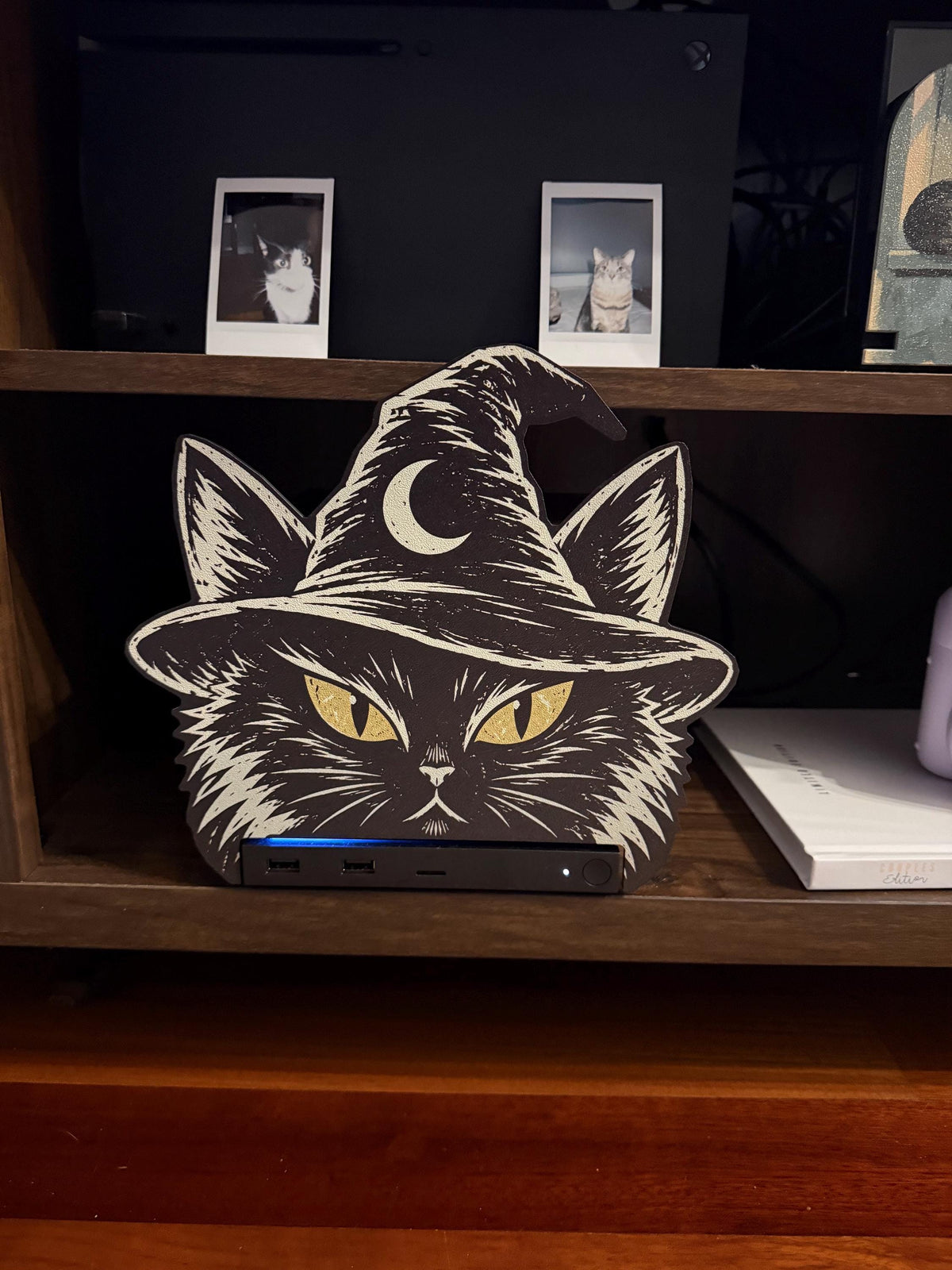 Steam Machine Faceplate Black Cat Witch Hat, Halloween Witchy Cat Magnetic Plate, UV Printed Console Cover, Spooky Gamer Gift, black cat witch hat faceplate installed on the Steam Machine on a wooden shelf with a white book beside it, two instant cat photo prints on the shelf above