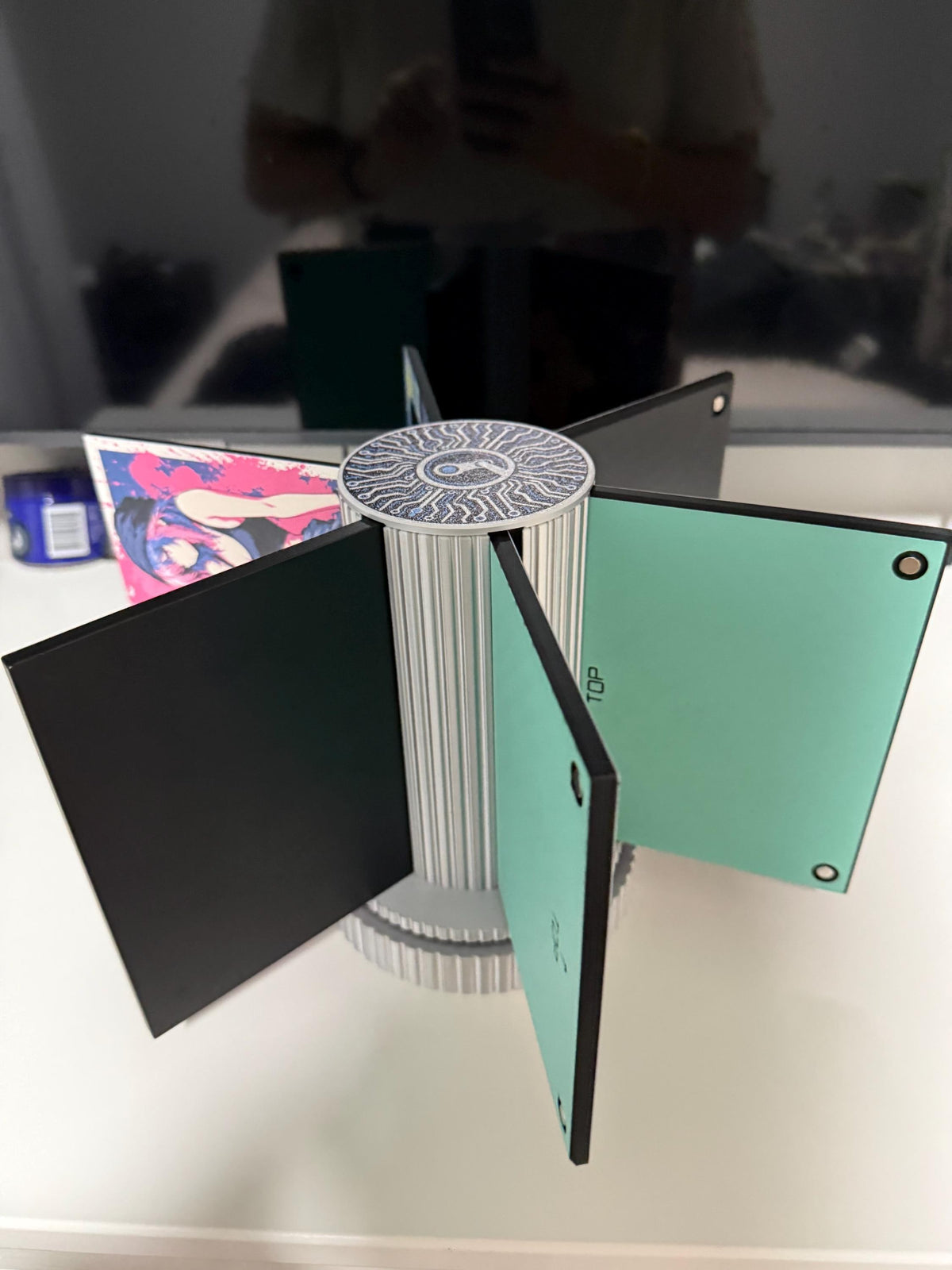 Steam Machine Faceplate Organizer, Spinning 3D Printed Display Stand, Rotating Plate Holder, Gamer Desk Setup, Gift for Gamer, Holds 6, eye-level view of the organizer with its six arms fanned out holding faceplates, showing the blank mint green back of one plate, on a white desk with a blurred monitor behind