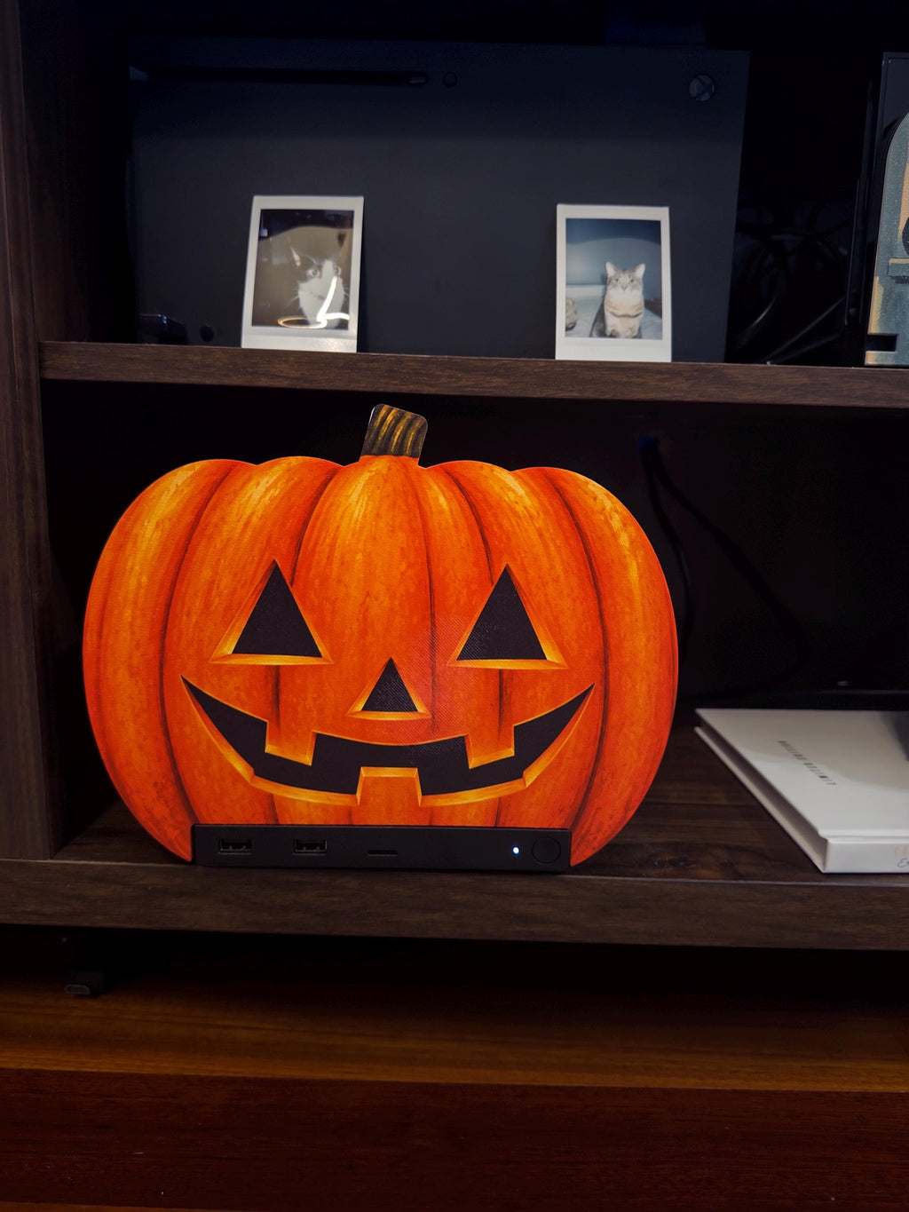 Steam Machine Faceplate Halloween Pumpkin, Classic or Cute Jack o Lantern Magnetic Plate, UV Printed Console Cover, Spooky Gamer Gif, classic carved jack-o-lantern pumpkin faceplate installed on the Steam Machine on a wooden shelf beside a white book, with framed cat photos on the shelf above