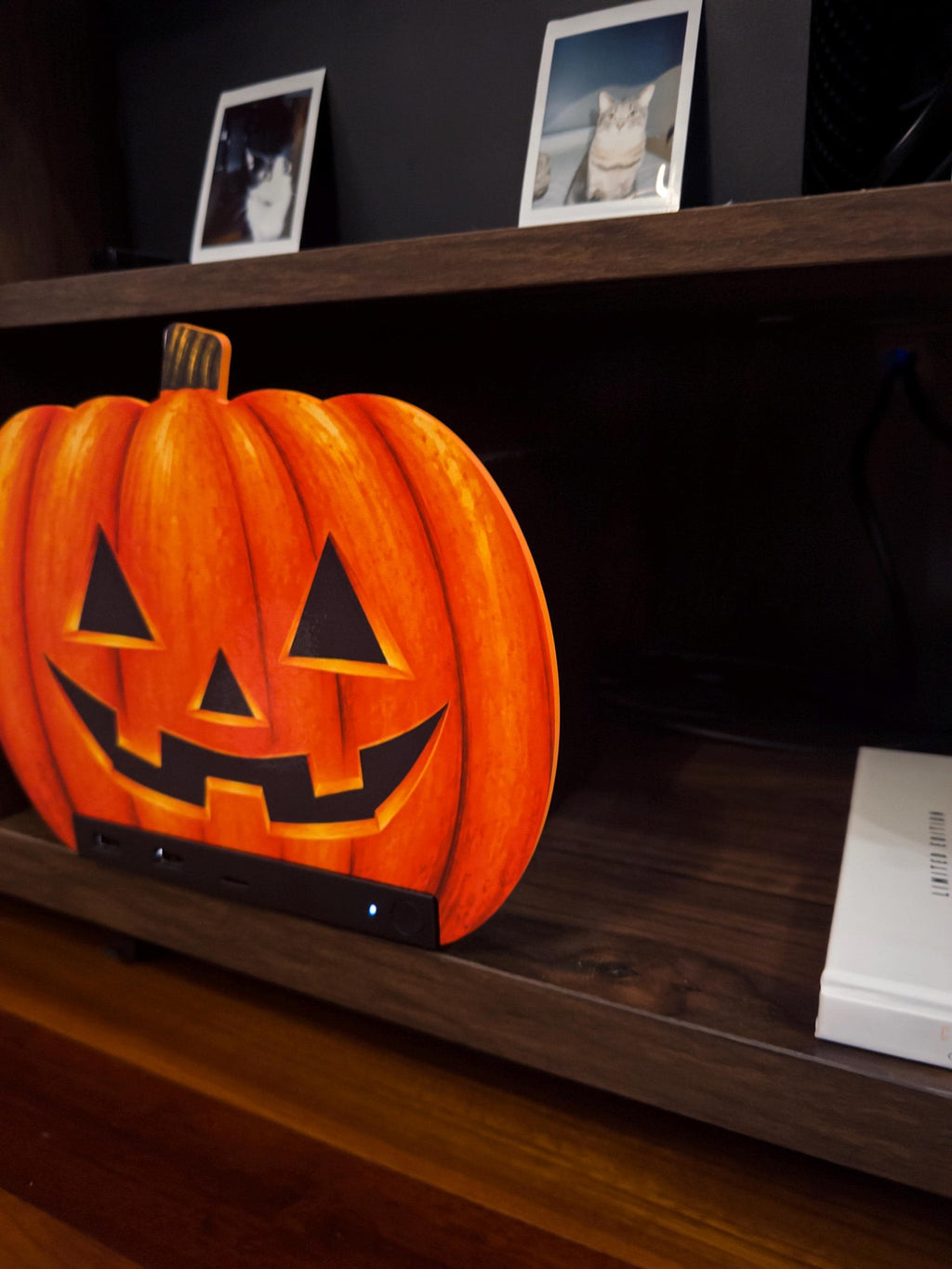 Steam Machine Faceplate Halloween Pumpkin, Classic or Cute Jack o Lantern Magnetic Plate, UV Printed Console Cover, Spooky Gamer Gif, close view of the classic carved jack-o-lantern pumpkin faceplate installed on the Steam Machine on a dark wooden shelf, with a white book beside it and framed cat photos on the top shelf