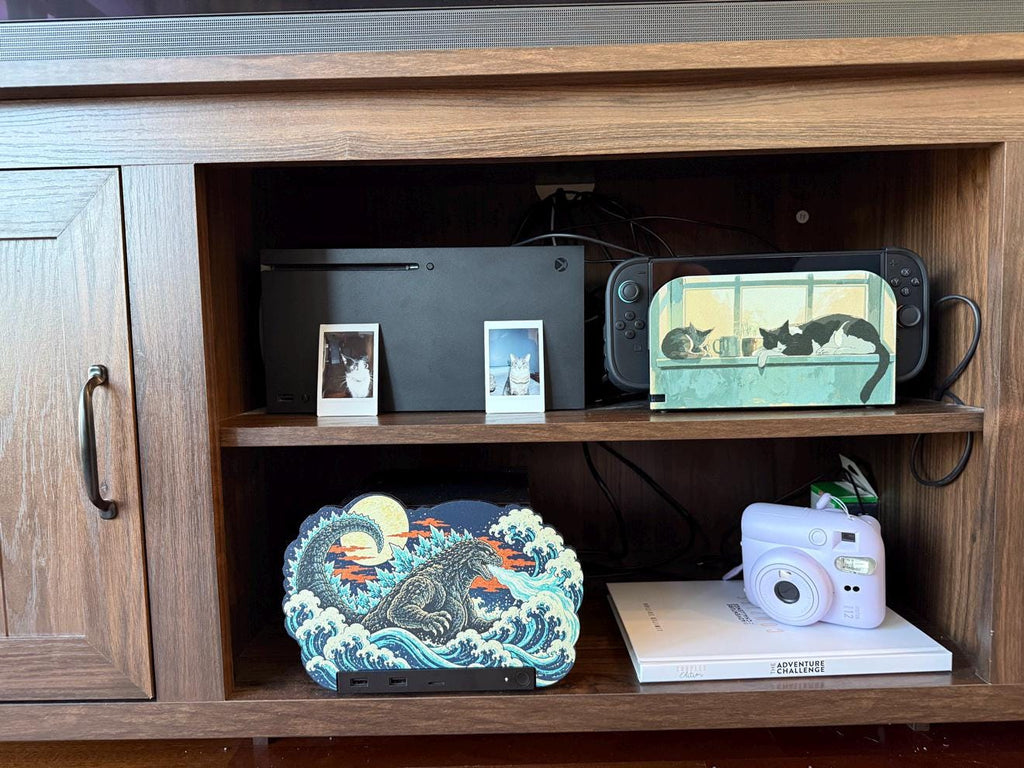 Steam Machine Faceplate, Custom Faceplate, Godzilla Kaiju Plate XL Oversized, Magnetic Console Cover, Monster Gamer Gift, Japan Wave Decor, Godzilla kaiju XL faceplate installed on the lower shelf of a wooden media cabinet, beside a white book with a lavender instant camera, with game consoles and cat photo prints on the shelf above
