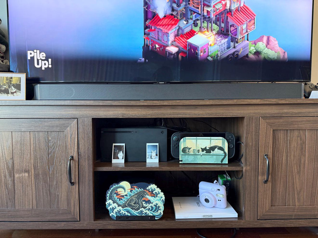 Steam Machine Faceplate, Custom Faceplate, Godzilla Kaiju Plate XL Oversized, Magnetic Console Cover, Monster Gamer Gift, Japan Wave Decor, Godzilla kaiju XL faceplate installed on the open shelf of a wooden TV console beneath a large television and soundbar, beside a white book with a lavender instant camera