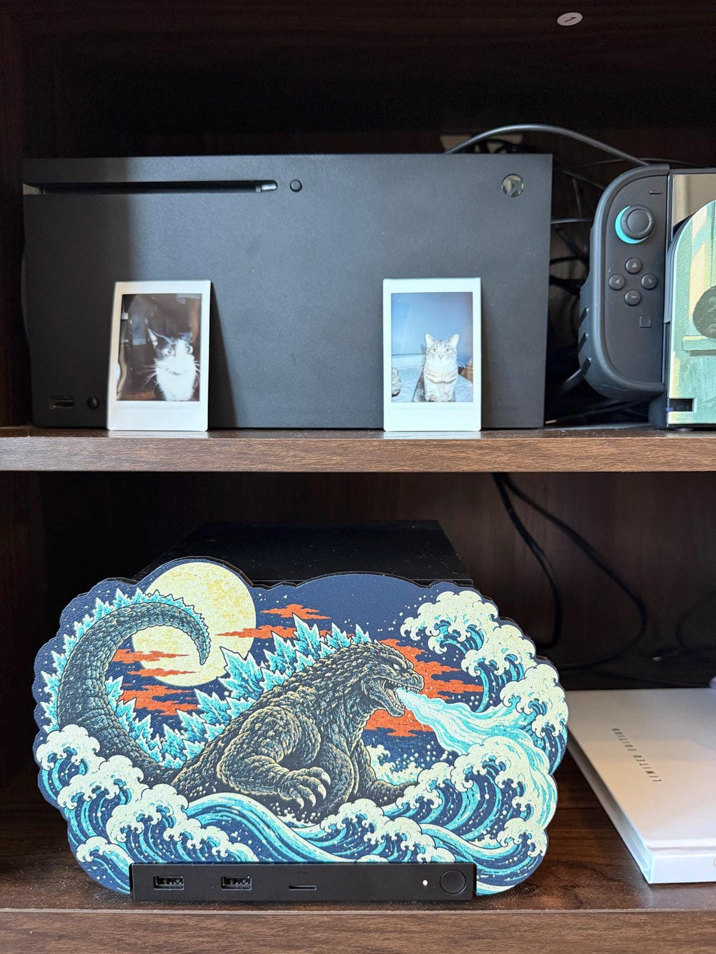 Steam Machine Faceplate, Custom Faceplate, Godzilla Kaiju Plate XL Oversized, Magnetic Console Cover, Monster Gamer Gift, Japan Wave Decor, Godzilla kaiju XL faceplate installed on the lower shelf of a wooden media console below an Xbox with two cat photo prints, beside a white book