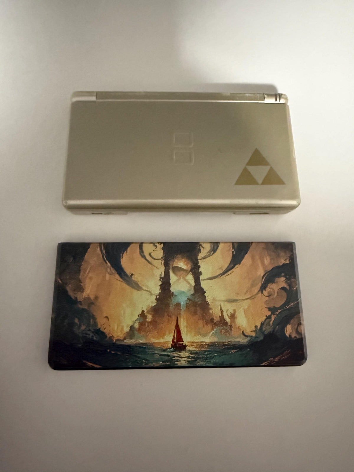 DS Lite Custom Lid, Full Color UV Printed Snap On Cover, Top Shell Faceplate for Original DS Lite, Your Own Image, Interchangeable Lid, uninstalled fantasy sea and glowing tower artwork lid shown next to a silver DS Lite console with a Zelda Triforce decal on its lid, on a plain light background