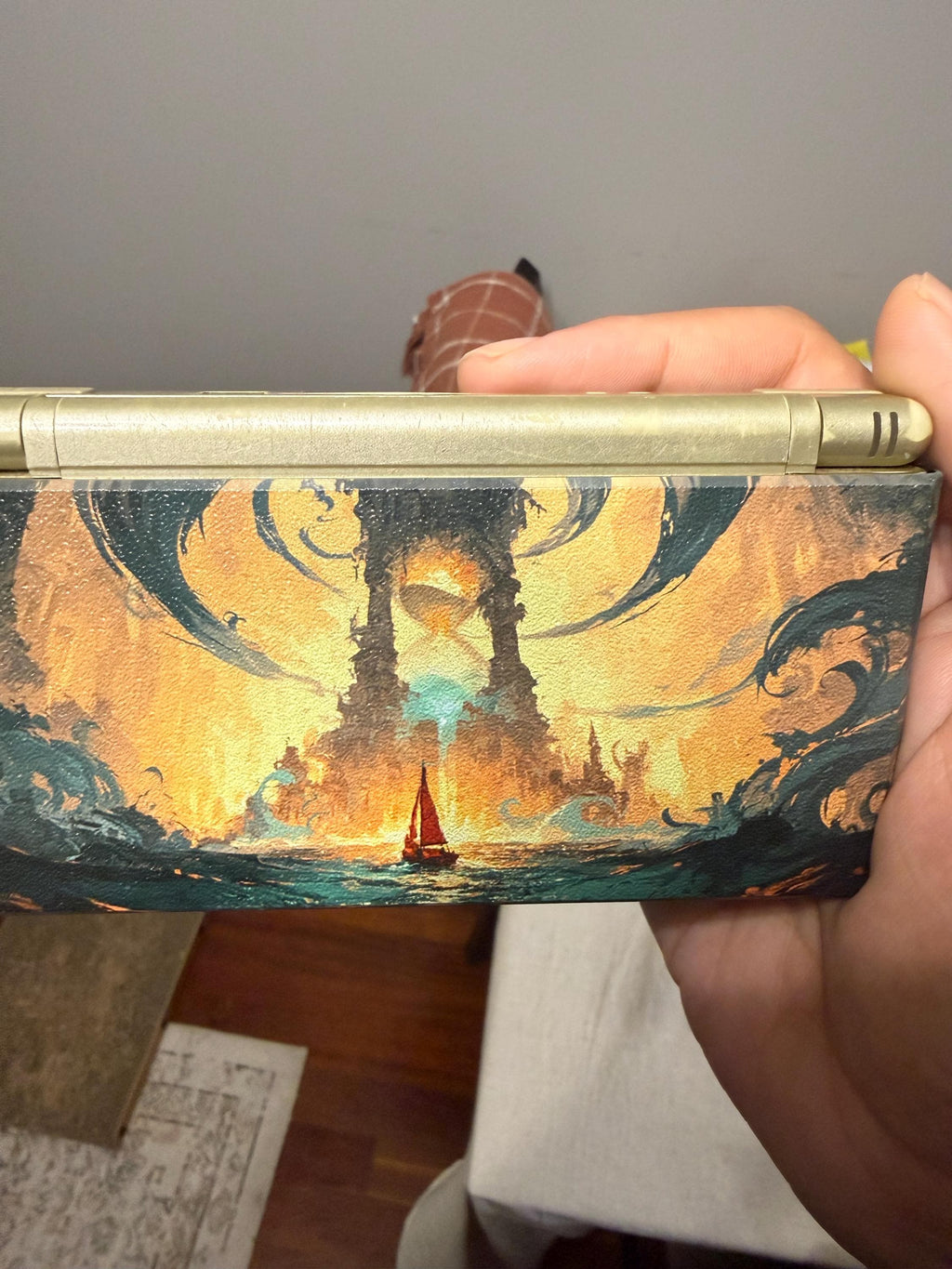 DS Lite Custom Lid, Full Color UV Printed Snap On Cover, Top Shell Faceplate for Original DS Lite, Your Own Image, Interchangeable Lid, hand holding a gold DS Lite console with the fantasy sea, glowing tower and sailboat artwork lid installed, shown from the back