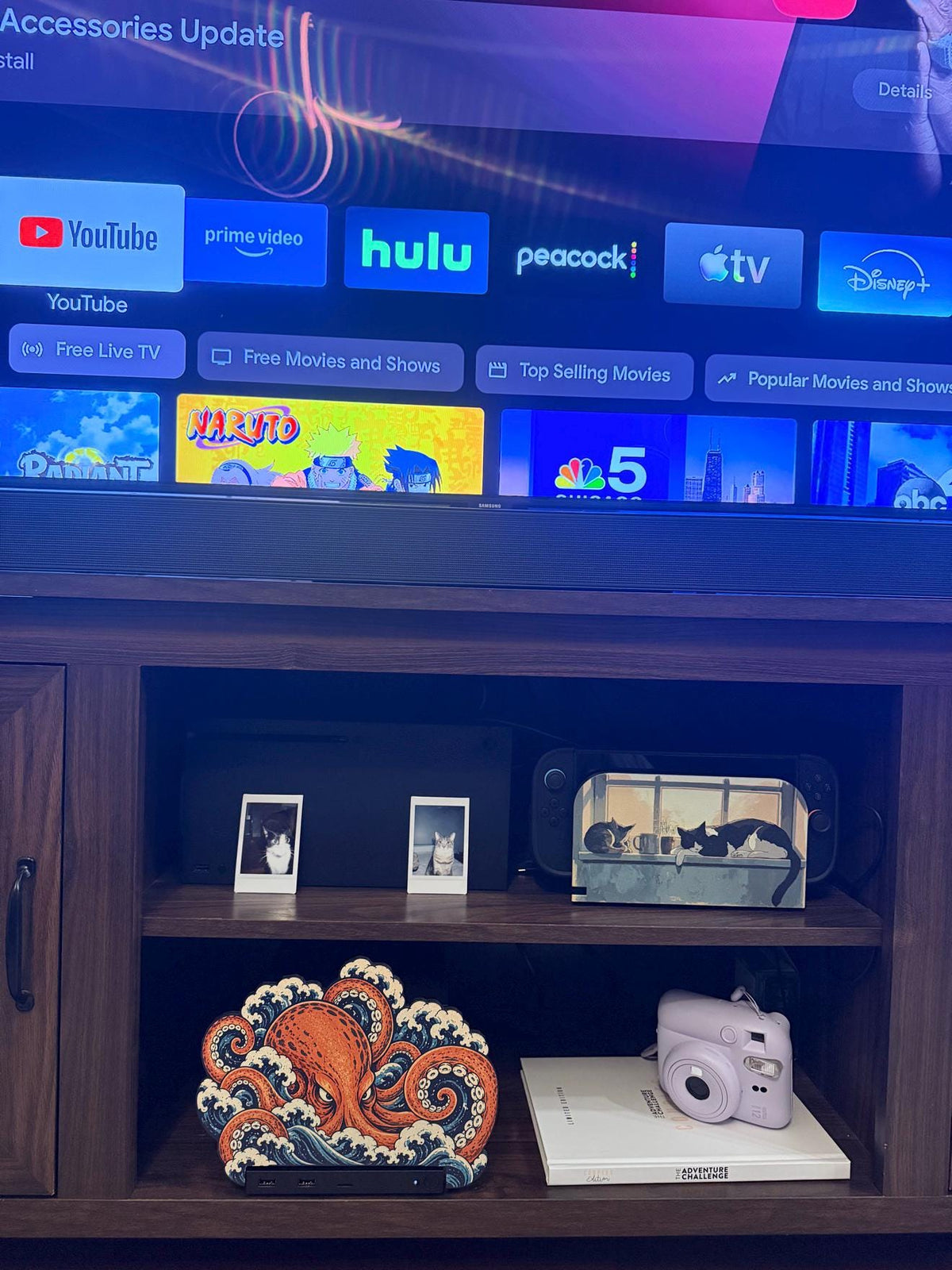 Steam Machine Faceplate, Custom Faceplate, Kraken Kaiju Plate XL Oversized, Magnetic Console Cover, Octopus Gamer Gift, Japan Wave Decor, Kraken kaiju XL faceplate installed on the lower shelf of a wooden TV console below a television showing streaming app icons, beside a white book with a pink instant camera