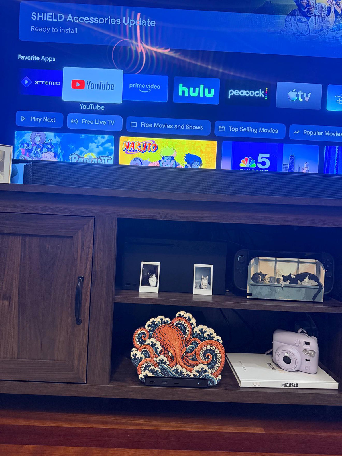 Steam Machine Faceplate, Custom Faceplate, Kraken Kaiju Plate XL Oversized, Magnetic Console Cover, Octopus Gamer Gift, Japan Wave Decor, Kraken kaiju XL faceplate installed on the lower shelf of a wooden TV console beneath a television showing a streaming home screen, with a white book and light pink instant camera beside it