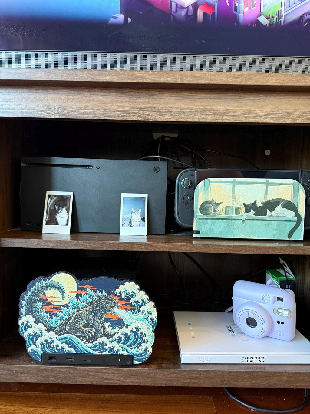 Steam Machine Faceplate, Custom Faceplate, Godzilla Kaiju Plate XL Oversized, Magnetic Console Cover, Monster Gamer Gift, Japan Wave Decor, Godzilla kaiju XL faceplate installed on the wooden TV console shelf beside a white book with a lavender instant camera, with an Xbox and Nintendo Switch on the shelf above