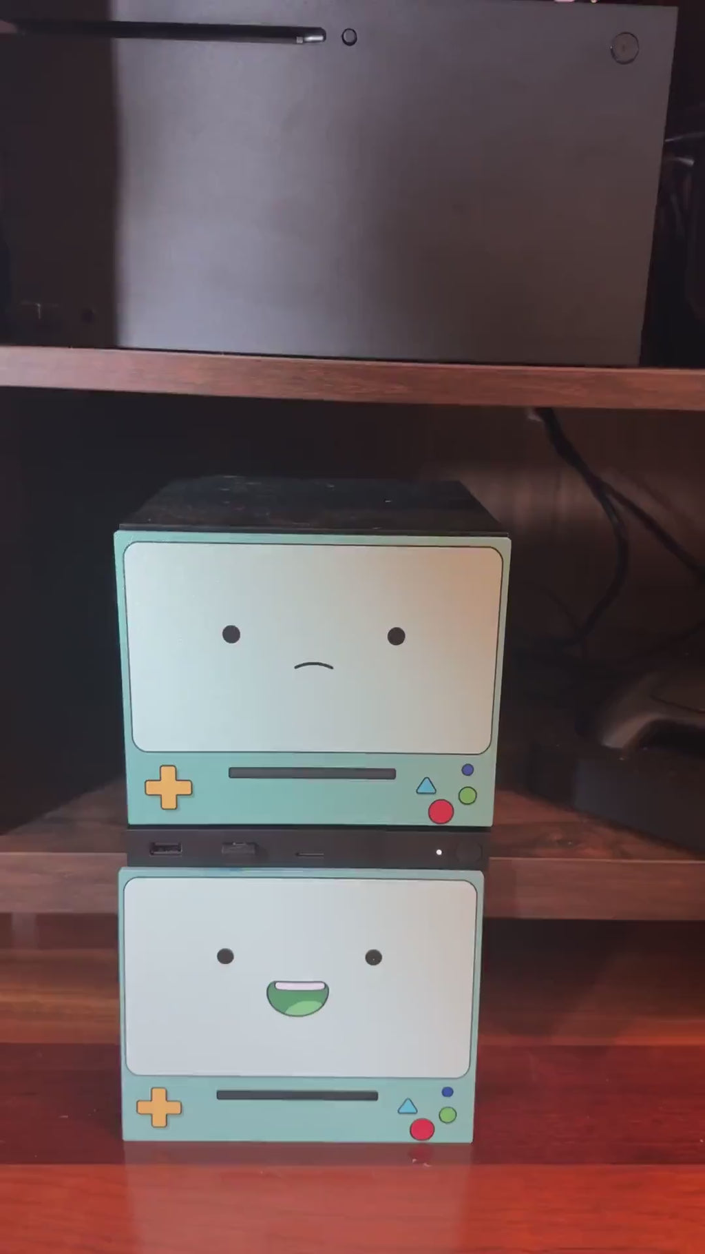 Robot Face Console Skin 2-Pack, Happy Sad Expression, Kawaii Gaming Setup Upgrade, video showing hands attaching the happy grinning expression skin onto the console on a wooden shelf